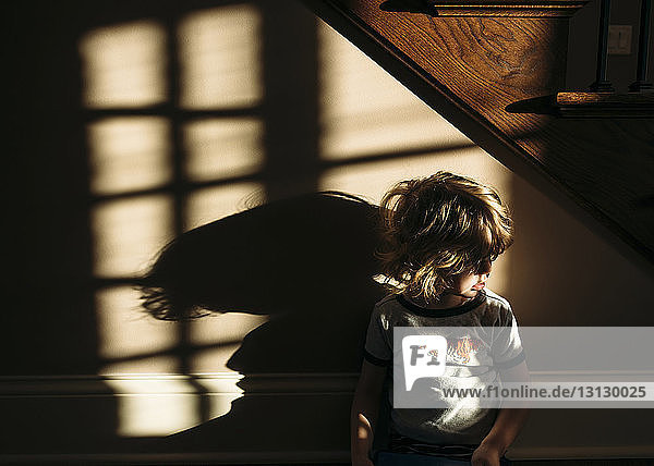 Junge sitzt zu Hause unter einer Treppe