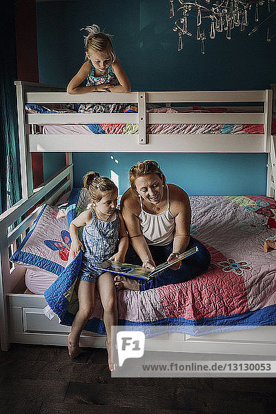 Mother reading book while sitting with daughters on bunkbed at home