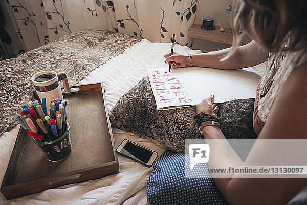 Beschnittenes Bild eines Künstlers  der zu Hause auf dem Bett sitzend Kalligrafie macht