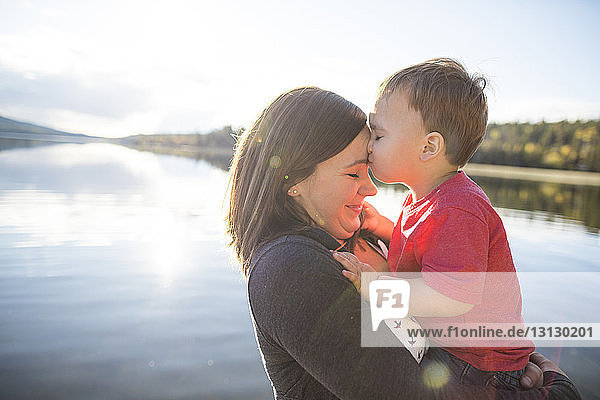 Son kissing mother on forehead against lake