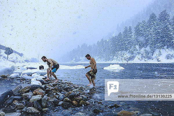 Men walking on stones in river during snowfall