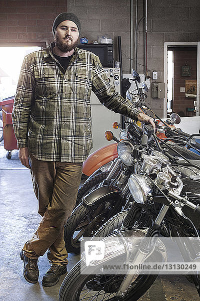 Porträt eines selbstbewussten Mechanikers  der bei Motorrädern in der Autowerkstatt steht