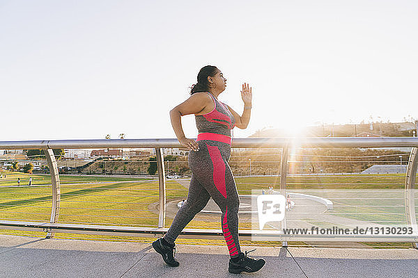 Seitenansicht einer Frau  die auf einem erhöhten Gehweg gegen den klaren Himmel joggt
