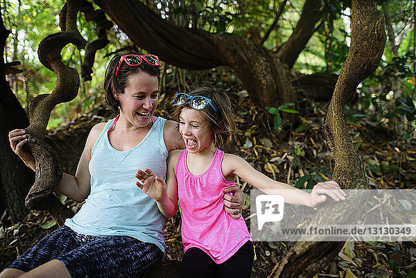 Cheerful mother and daughter sitting on tree trunk