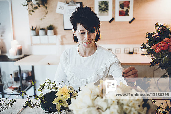 Lächelnder Florist arrangiert Blumen auf Blumenschaum bei Tisch im Laden