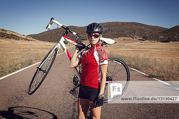 Porträt einer selbstbewussten Radfahrerin  die ein Fahrrad auf der Landstraße trägt