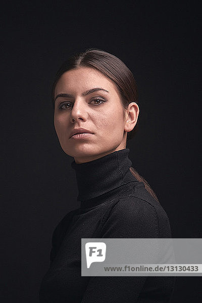 Porträt einer selbstbewussten Frau vor schwarzem Hintergrund stehend