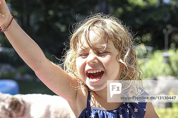Nahaufnahme eines glücklichen Mädchens mit erhobener Hand  das schreiend im Hof steht