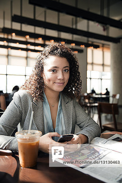 Porträt einer Geschäftsfrau  die ein Smartphone am Café-Tisch hält