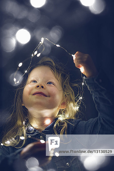 Happy girl playing with illuminated string lights during night