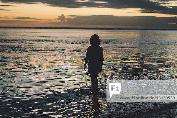 Silhouettenfrau steht am Strand vor bewölktem Himmel bei Sonnenuntergang