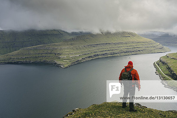 Wanderer mit Rucksack schaut auf Aussicht  während er auf einer Klippe vor stürmischen Wolken steht