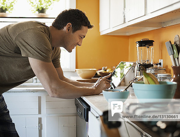 Lächelnder Mann benutzt Tablette  während er zu Hause in der Küche steht