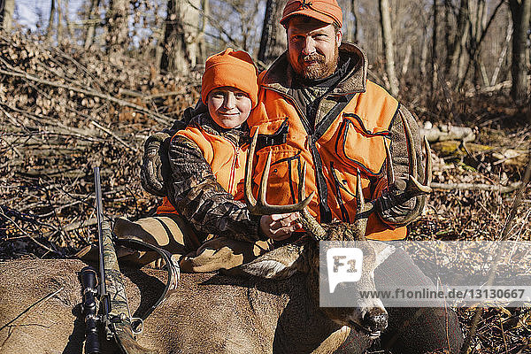 Portrait of father and daughter with dead deer on field