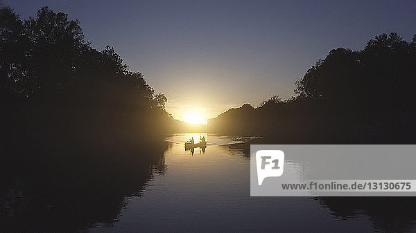 Vater und Sohn fahren bei Sonnenuntergang auf dem See Boot