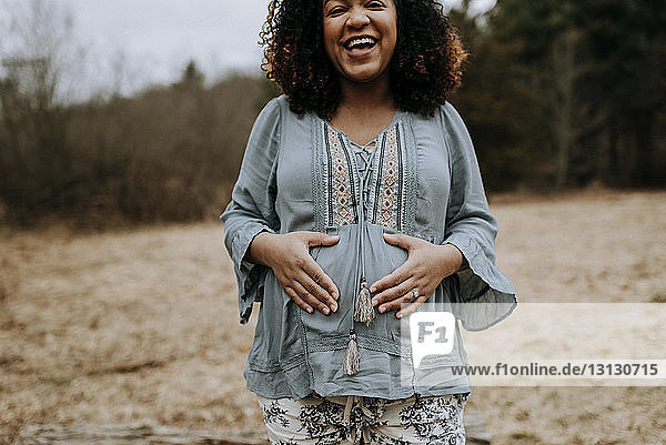 Porträt einer glücklichen schwangeren Frau  die den Bauch berührt  während sie im Wald steht