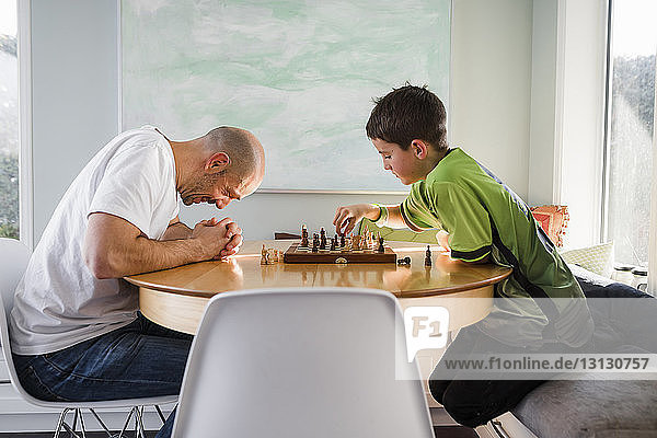 Vater mit Sohn spielt zu Hause am Tisch Schach