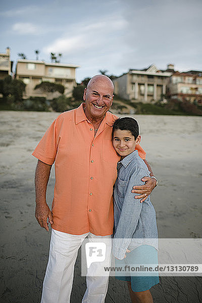 Porträt eines Großvaters mit Enkel  der bei Sonnenuntergang am Strand steht