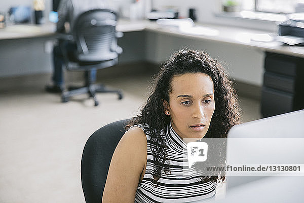 Geschäftsfrau benutzt Computer  während ein männlicher Kollege im Hintergrund