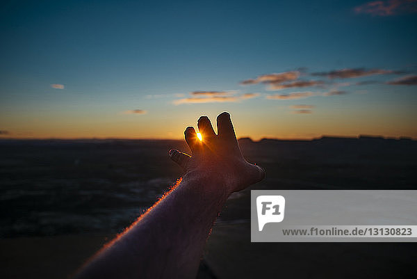 Abgehackte Hand eines Mannes  der bei Sonnenuntergang über die Silhouette der Landschaft gegen den Himmel gestikuliert