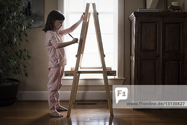 Side view of girl drawing on artist's canvas while standing at home