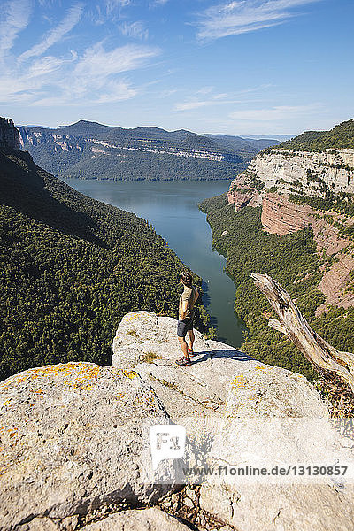 Side view of male hiker looking at lake while standing on mountain against sky during sunny day