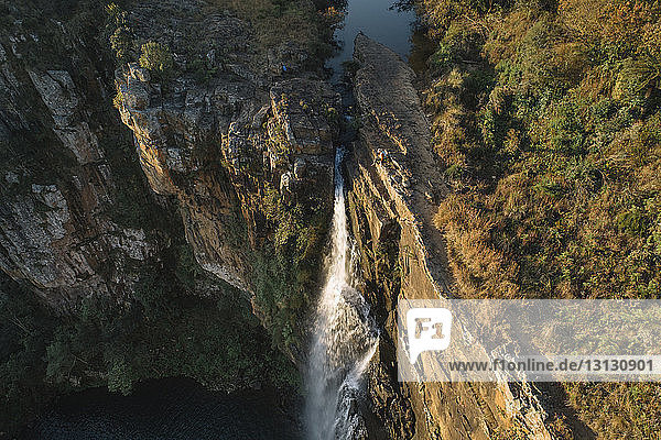 Luftaufnahme einer Frau  die über einem Wasserfall auf einem Berg im Wald sitzt