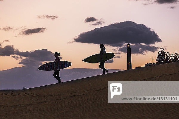 Scherenschnittfreunde mit Surfbrettern bei Sonnenuntergang in der Wüste vor bewölktem Himmel
