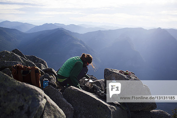 Hiker boiling water while crouching on rocks against mountains