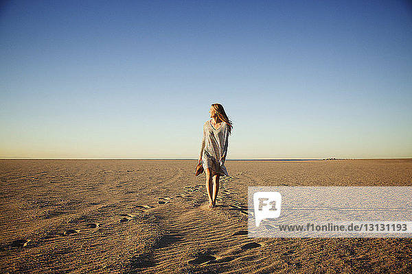 Carefree woman walking on beach against clear blue sky during sunset