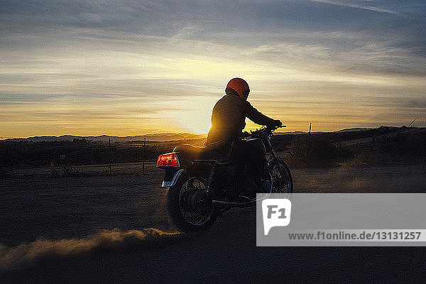 Man riding motorcycle on field against sky during sunset
