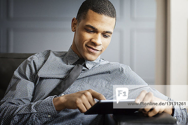 Businessman using tablet computer while sitting on sofa in office