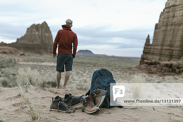 Full length of hiker looking at view with shoes ad backpack in foreground on desert