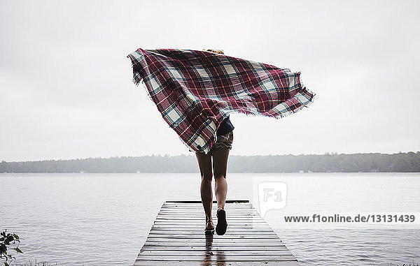 Rückansicht einer sorglosen Frau  die mit einer Decke auf dem Pier über die Kawartha-Seen gegen den klaren Himmel rennt