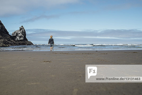 Junge in voller Länge mit Stock in der Hand  während er auf Sand am Strand gegen den Himmel läuft