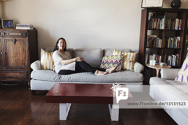 Portrait of woman holding mobile phone while sitting on sofa at home