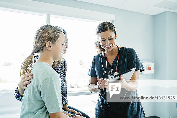 Cheerful pediatrician showing tablet computer to mother and daughter in medical examination room
