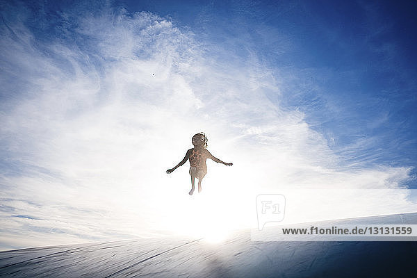 Glückliches Mädchen springt bei Sonnenschein auf Sportrampe gegen den Himmel