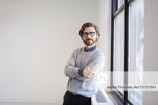 Portrait of confident businessman with arms crossed standing by window in new office