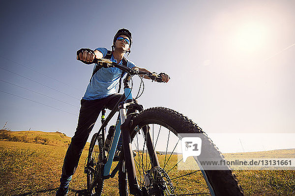 Niedrigwinkelansicht eines männlichen Athleten auf dem Fahrrad im Feld vor klarem Himmel