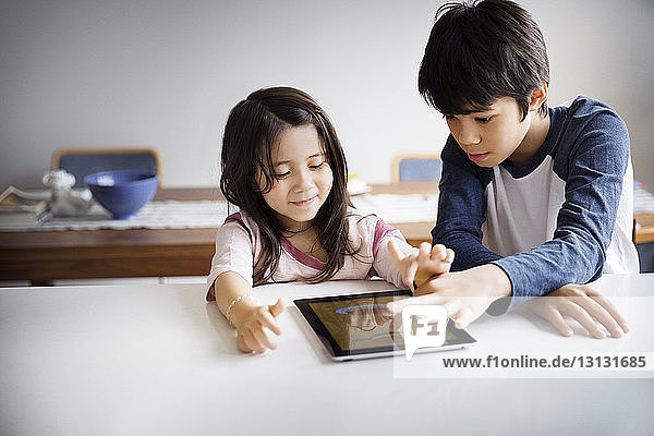 Geschwister benutzen zu Hause ein digitales Tablett auf dem Tisch
