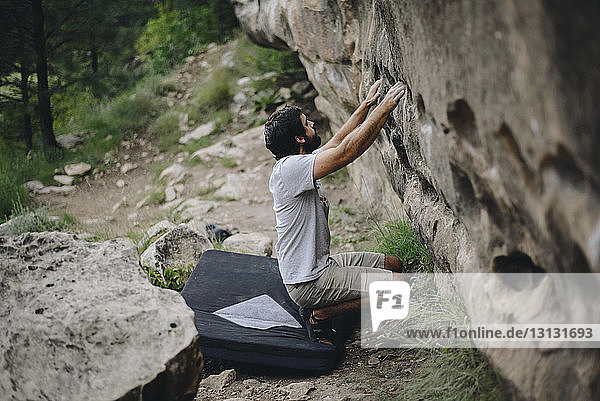 Man crouching on bouldering mat while preparing for rock climbing at forest