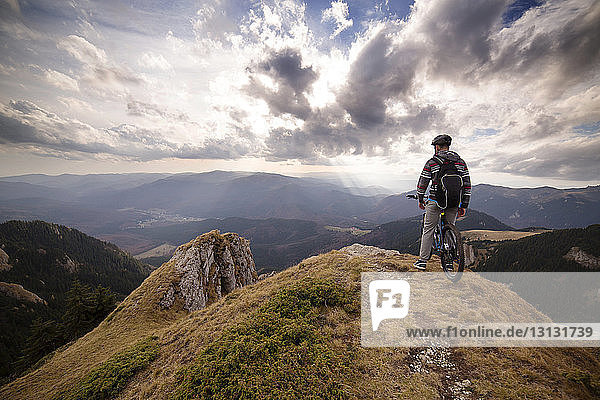 Rear view of man on bicycle on mountain against cloudy sky