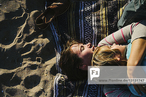 Draufsicht einer Frau  die ihre Tochter umarmt  während sie auf einem Strandtuch liegt