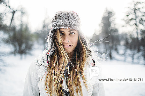 Porträt einer lächelnden Frau mit Pelzmütze auf schneebedecktem Feld
