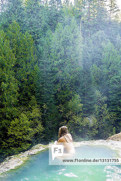 Hochwinkelaufnahme einer Frau  die in einer heissen Quelle im Wald schwimmt