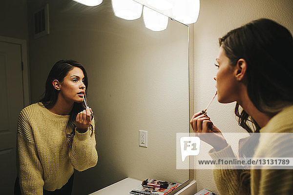 Woman applying lip gloss reflecting on mirror at home