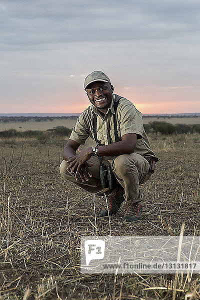 Porträt eines glücklichen Mannes  der auf einem Grasfeld im Serengeti-Nationalpark kauert