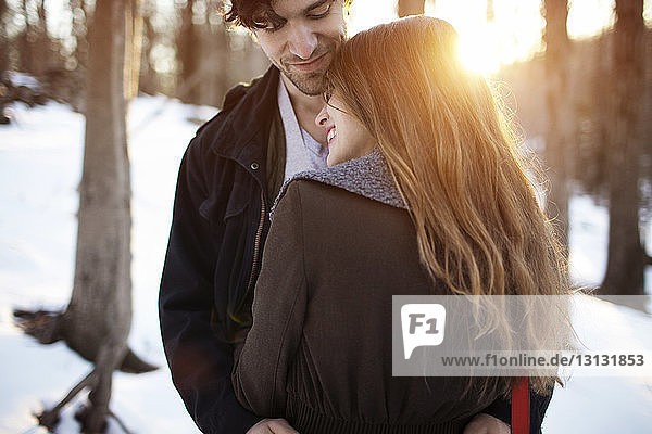 Rückansicht einer glücklichen Frau,  die den Mann im Winter umarmt