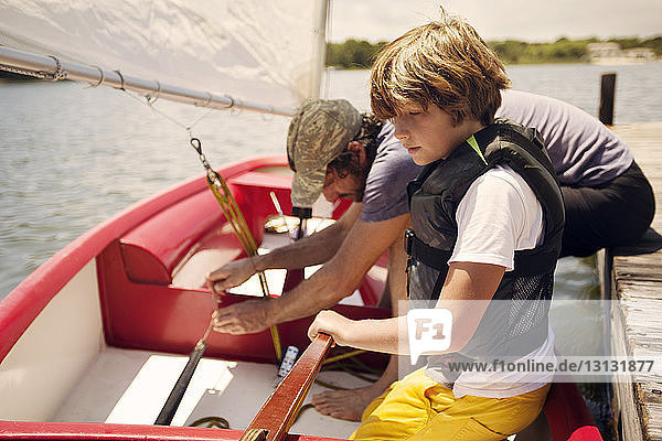 Vater und Sohn bereiten sich auf das Bootfahren im See gegen den Himmel vor